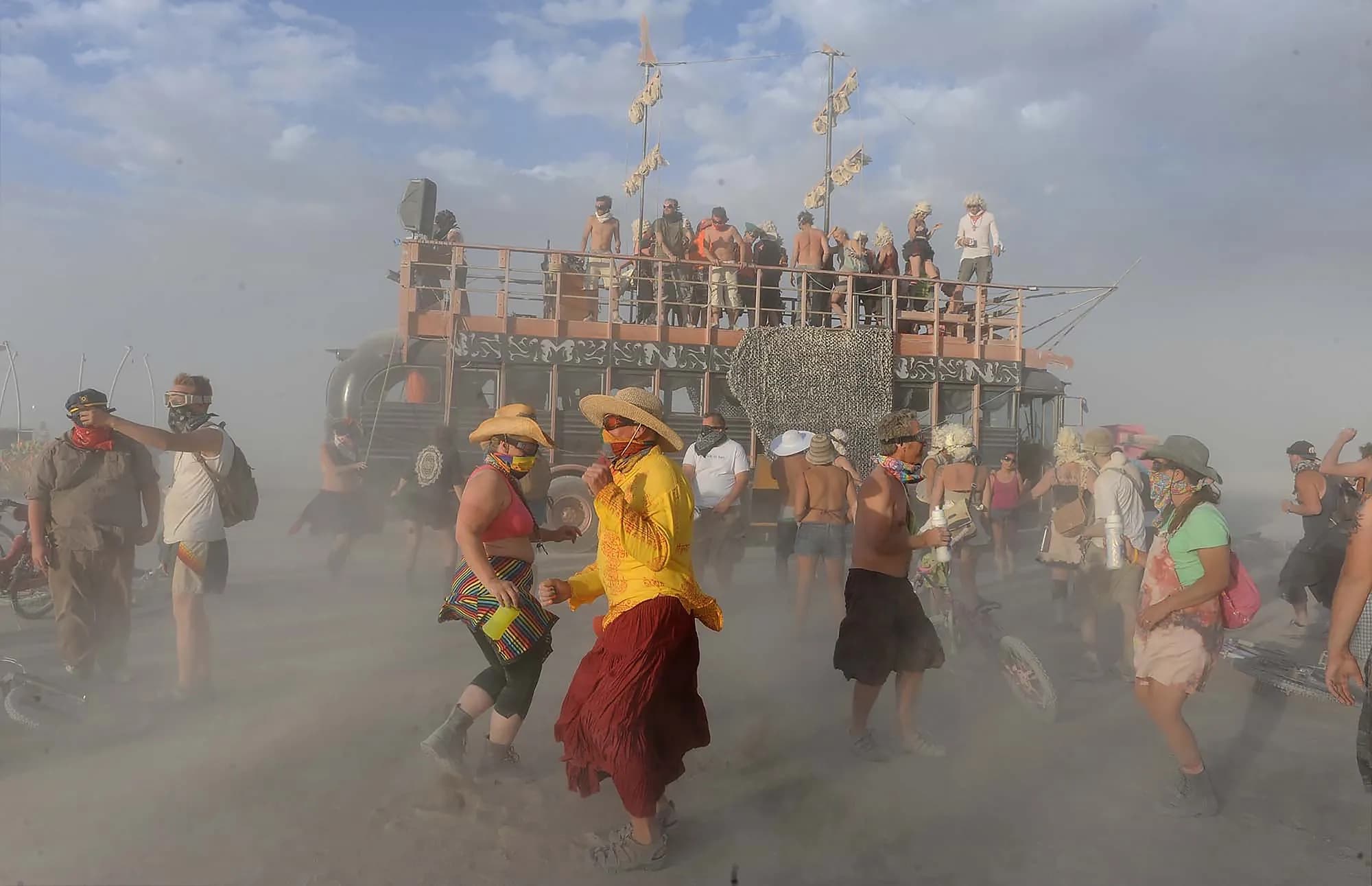 People in dust masks and goggles walking through a daytime whiteout on the playa.