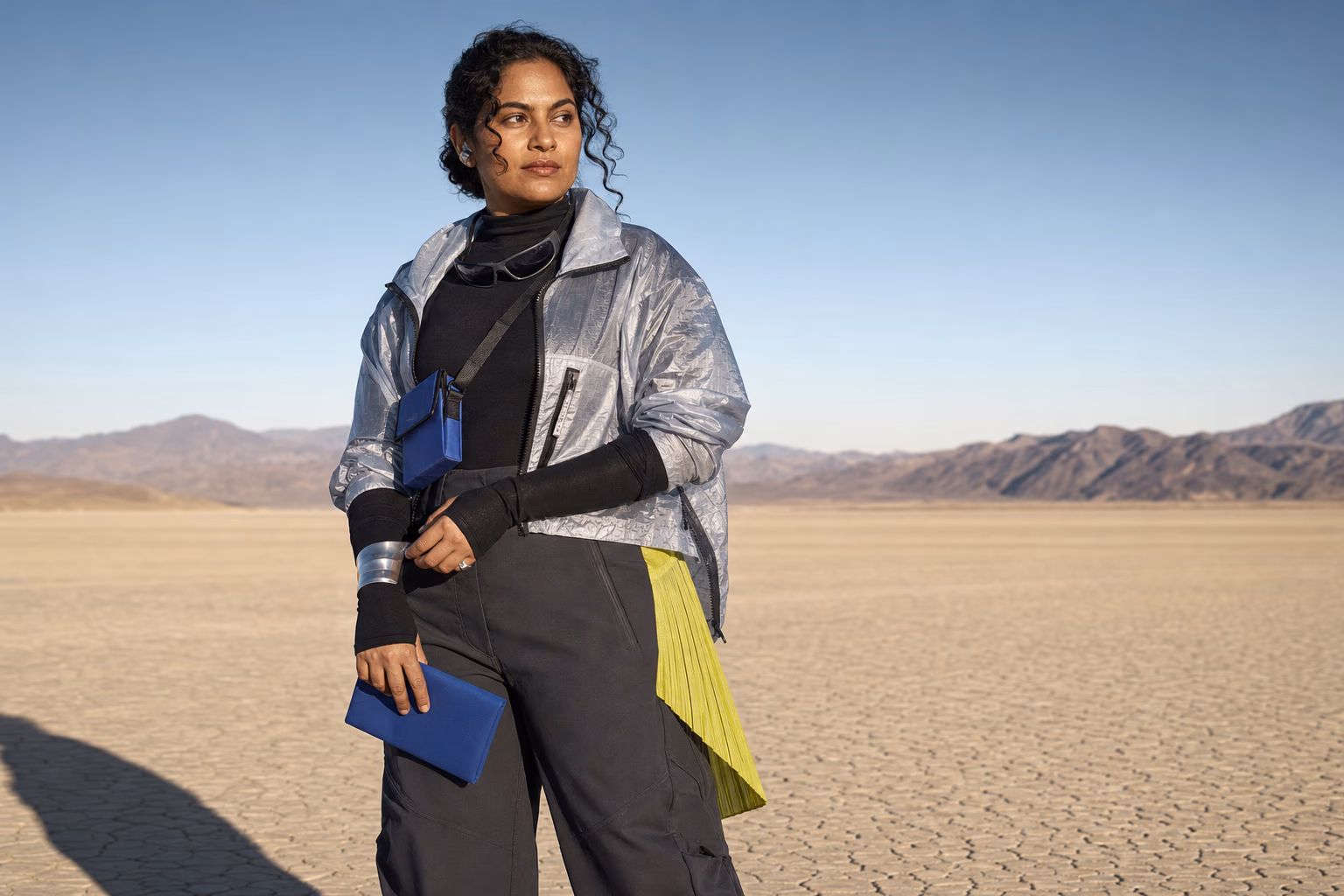 South Asian stylist in a practical silver shell, black technical layers, and citron and cobalt accents in the desert